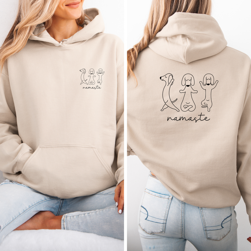 Beigefarbener Hoodie mit drei Hunden in Yoga-Posen und dem Schriftzug „Namaste“, vorne klein und hinten groß, von einer Frau getragen.