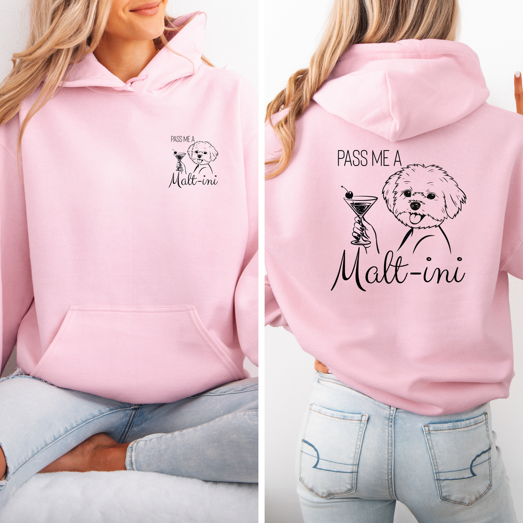 Rosafarbener Hoodie mit Malteser-Illustration und Schriftzug „Pass me a Malt-ini“ vorne klein und hinten groß; Frau sitzt und trägt den Hoodie.