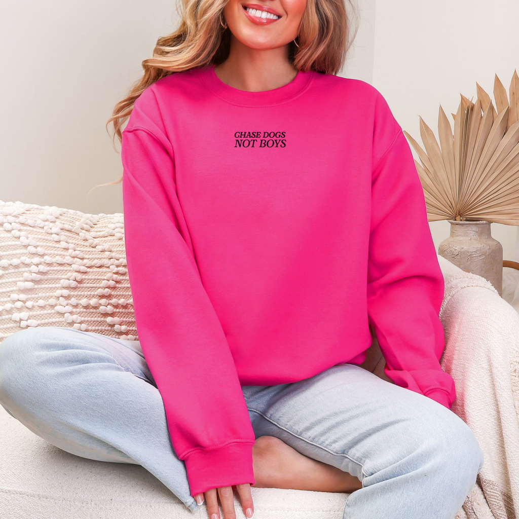 Pinker Oversize-Sweater mit kleinem schwarzen „Chase Dogs Not Boys“-Schriftzug vorne auf der Brust, getragen von einer Frau.
