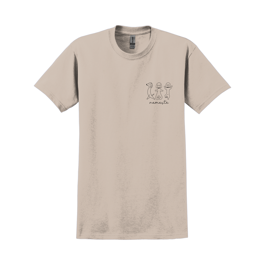 Beiges T-Shirt mit kleinem Frontprint „Namaste“ und drei hundeartigen Figuren in Yoga-Posen; Produktfoto vor weißem Hintergrund.